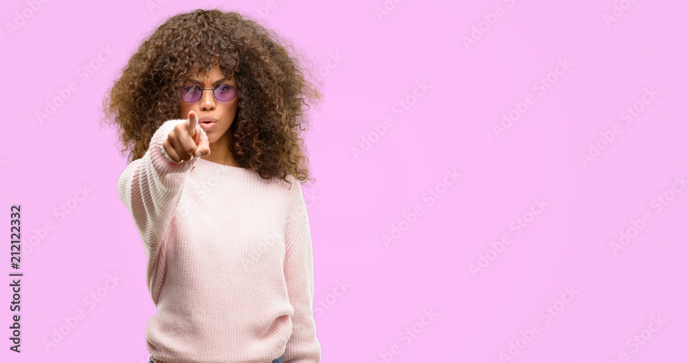 Sticker african american woman wearing a pink sweater pointing with finger to the camera and to you, hand si