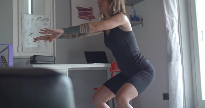 young tattooed woman doing squats exercise during home fitness sport workout .Living room domestic training. 4k slow motion video