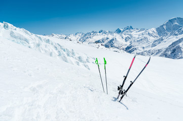 A pair of skis and ski poles stick out in the snow on the mountain slope of the Caucasus against...