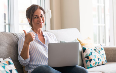 Middle aged woman using laptop in the sofa pointing with hand and finger up with happy face smiling