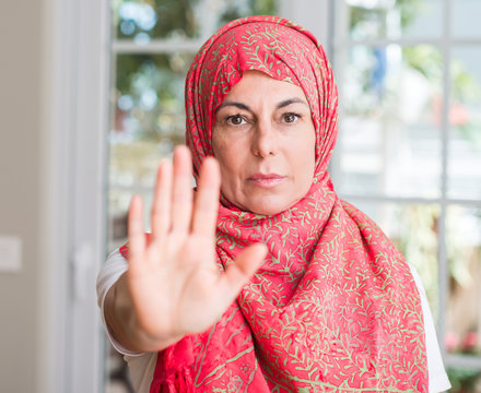 Middle aged muslim woman wearing hijab with open hand doing stop sign with serious and confident expression, defense gesture