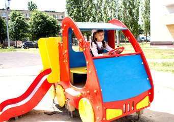 A teenage girl playing on the playground.  Sits at the wheel of a toy car.