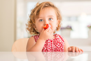 Beautiful blonde child with blue eyes eating strawberry at home. © Krakenimages.com