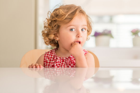 Beautiful blonde child with blue eyes eating candy and looking at the camera at home.