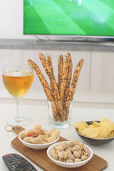 Football snacks with russian flag and football game on tv on the background Supporting national team concept Football fan food Beer, peanuts, pistacios, potato chips and tv remote control