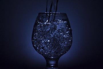Simple still-life photo of whisky glass, water jet and dim colour light
