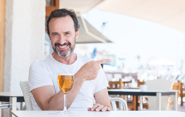 Handsome senior man drinking beer at restaurant very happy pointing with hand and finger to the side