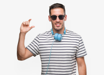 Naklejka premium Handsome young man wearing headphones smiling and confident gesturing with hand doing size sign with fingers while looking and the camera. Measure concept.