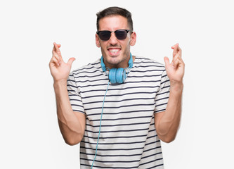 Naklejka premium Handsome young man wearing headphones smiling crossing fingers with hope and eyes closed. Luck and superstitious concept.