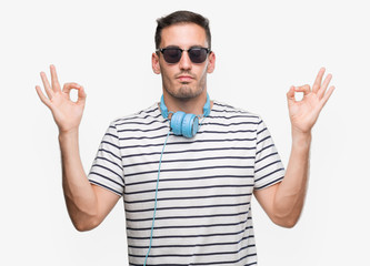 Naklejka premium Handsome young man wearing headphones relax and smiling with eyes closed doing meditation gesture with fingers. Yoga concept.