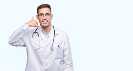 Fototapeta premium Handsome young doctor man smiling doing phone gesture with hand and fingers like talking on the telephone. Communicating concepts.
