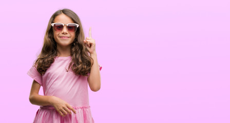 Brunette hispanic girl wearing sunglasses surprised with an idea or question pointing finger with happy face, number one