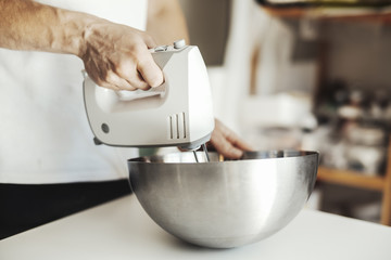 Metal bowl with mixer and hand on white table.