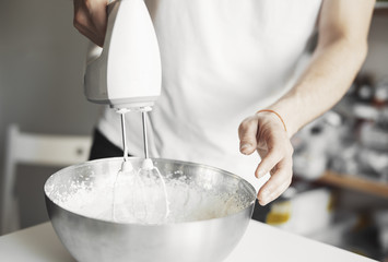 Cook uses metal bowl with mixer on white table.