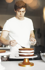 Young attractive man smearing sugar syrup on chocolate cake.