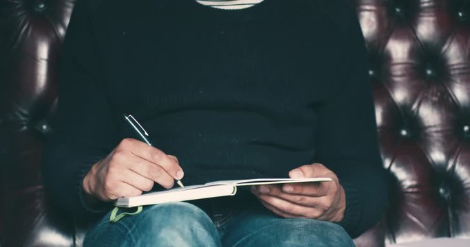 Young man sitting on sofa writing in notebook