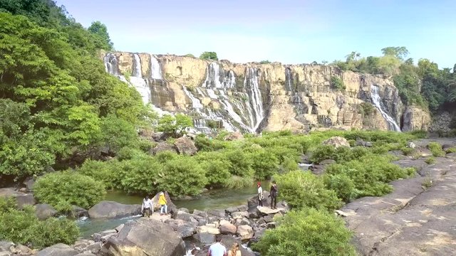 tourists walk on rocks watch waterfall Pongour
