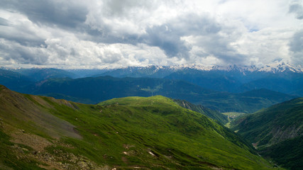 green slope against the background of snowy peaks of mountains and cloudy sky