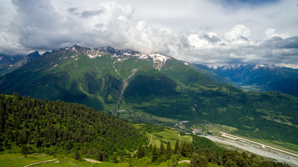 green slope, fprest and snowy peaks of mountains aerial view