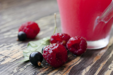Still life with ripe berries of raspberries, black corn and a glass of juice in the background