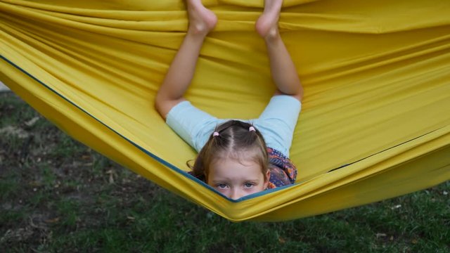 Girl child funny amuse enjoy lying in yellow hammock wagging barefooted legs