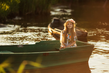Portrait of a beautiful little girl in a boat at sunset on the lake