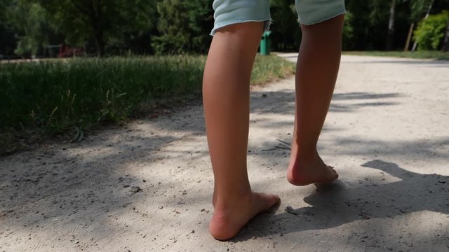 Child girl barefoot legs walk the ground park lane on hot summer day