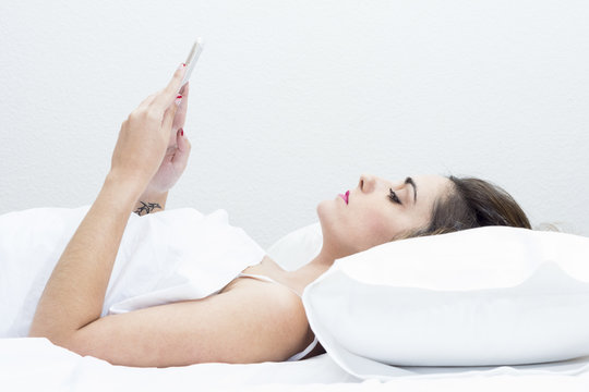 woman lying on a white bed face up with mobile hands