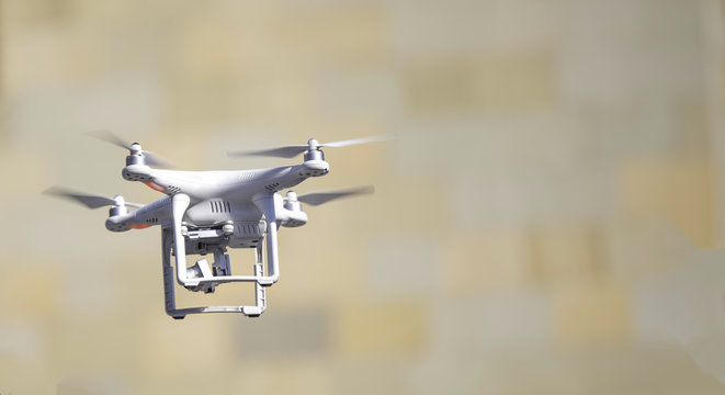 Flying Quadcopter Drone on yellow brown blurred background. Free copy text space.