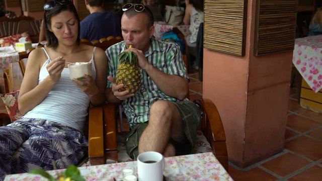 A man and a woman are sitting in a restaurant eating ice cream and drinking pineapple juice