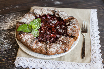 Сhocolate galette with cherries on brown wooden background. Summer pie.
