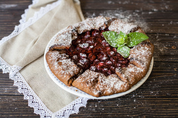 Сhocolate galette with cherries on brown wooden background. Summer pie.