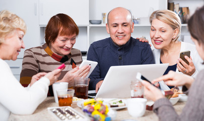 Fototapeta premium Smiling aged friends are sitting at table with notebook and talking about project