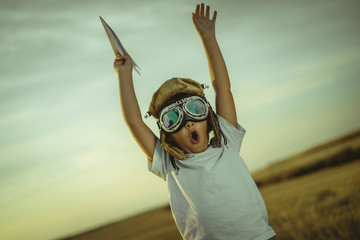 Happy boy at sunset playing at being aviator, he wears pilot glasses of airplanes and some...