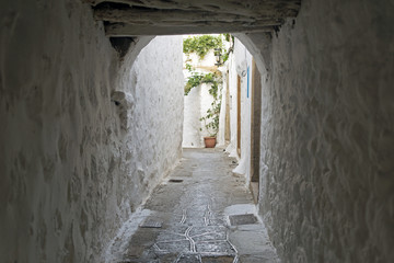 Fototapeta premium A view of a narrow street with arch and wooden windows and doors with white wall stone architecture of the island Patmos, Greece