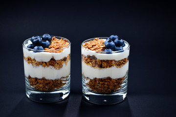 Homemade baked granola with yogurt and blueberries in a glass on a black background. Space for text or design.