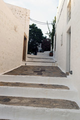 Naklejka premium A view of a narrow street with arch and wooden windows and doors with white wall stone architecture of the island Patmos, Greece