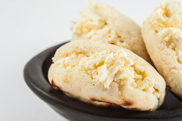 Colombian traditional white corn arepa stuffed with grated cheese in a black ceramic dish on black background
