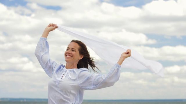 people and leisure concept - happy woman with shawl waving in wind on summer beach
