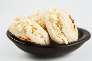 Colombian traditional white corn arepa stuffed with grated cheese in a black ceramic dish on black background