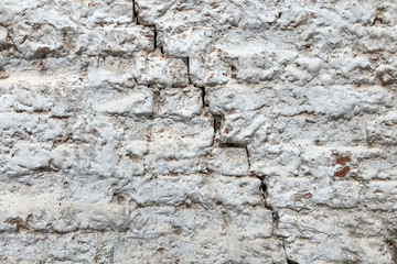 Old red brick wall covered with a white plaster and a large cracked. Texture background