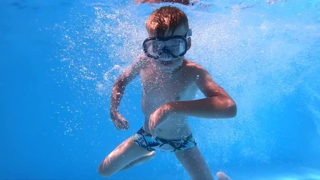 Children's games in the pool. Little, cute boy shows thumbs up under water. Slow motion.
