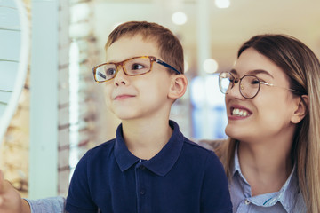 Mother with son choosing glasses in optics store.