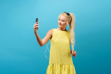 Fashion pretty cool girl makes self portrait on smartphone over blue background