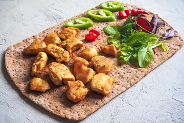 Pieces of fried chicken curry fillet on rye flatbread with vegetables.