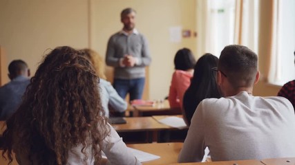 High school students multiethnic class are listening to teacher, raising hands and asking questions while educator is explaining new information. Learning and teaching concept. - Powered by Adobe