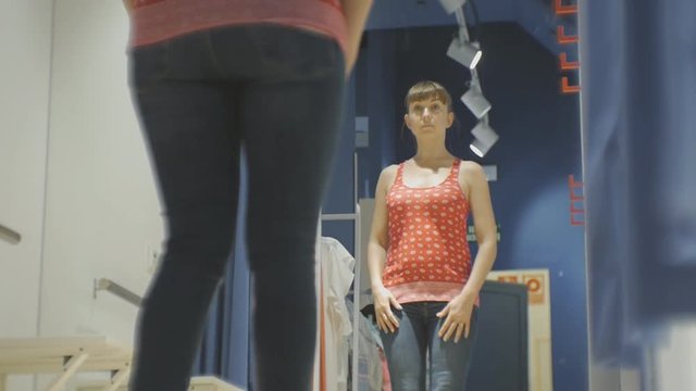Young woman trying on clothes. Low angle view of attractive caucasian female looking in the mirror spinning trying on red shirt and jeans in clothing store's fitting room