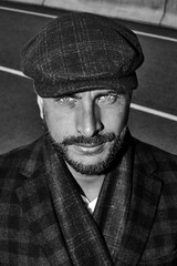 Beautiful monochrome portrait of a man in a cap. Cap of different colors and shapes. Autumn portrait, clouds behind and stormy sky. Scarf around the neck in the color of the cap. Face severe, serious.