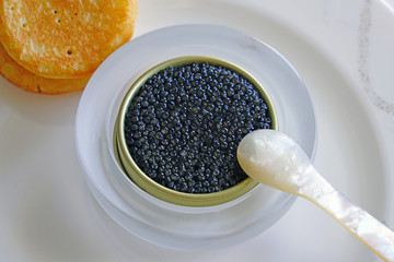 A tin of black sturgeon caviar with blinis and a mother-of-pearl spoon