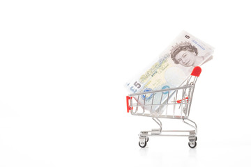 United Kingdom banknotes in small shopping trolley on white background. Finance concept.